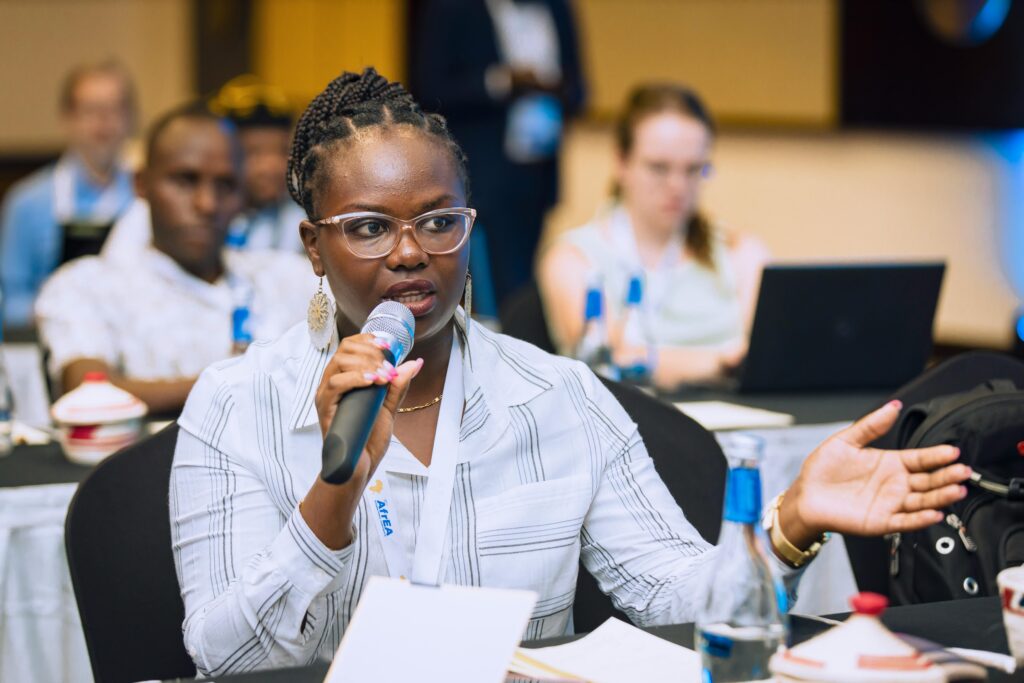 An attendee at a Research Engagement Network (REN) meeting participates in a discussion, holding a microphone and gesturing. Other participants are seen focused in the background.