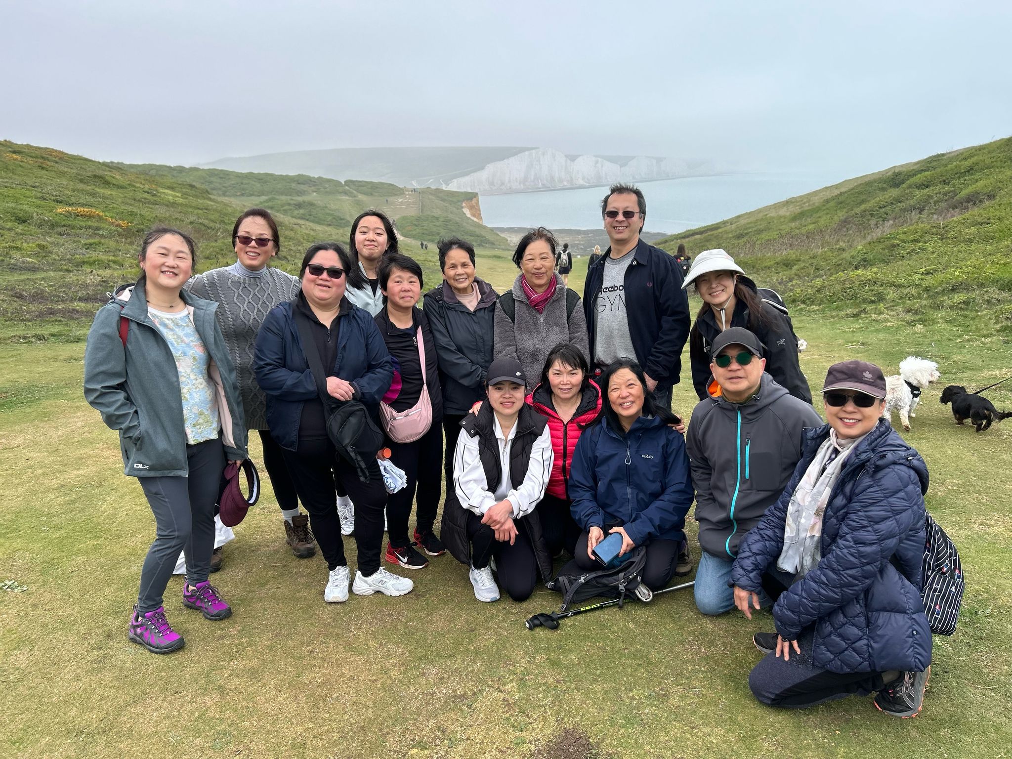 A group of fourteen people from an Asian background smile at the camera. To their back, there are the white cliffs on the South Downs National Park.