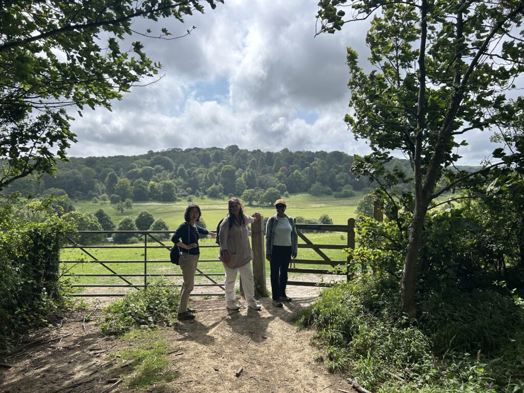 Two women, accompanied by Mebrak, smile at the camera in front of a gate in Stanmer Park. It's a sunny day.