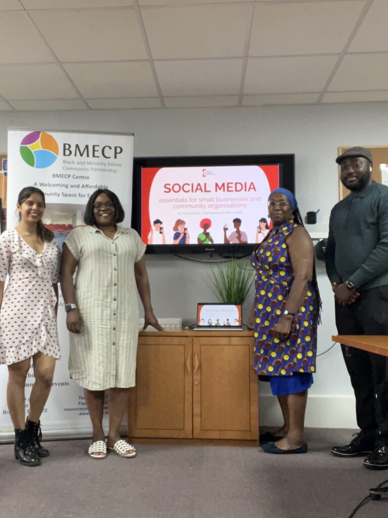 Four people standing in front of a presentation screen and a BMECP banner. The main text on the screen reads: "SOCIAL MEDIA essentials for small businesses and community organisations"
